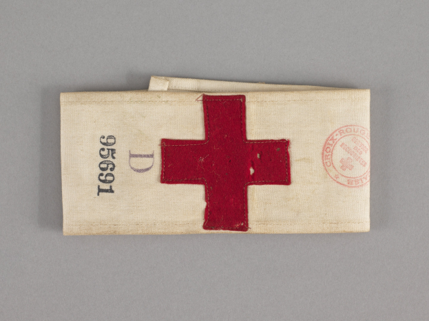 Ein rotes Kreuz-Ersthilfekit in einem Stoffbeutel mit Text und einem Stempel, das auf einer Oberfläche liegt.