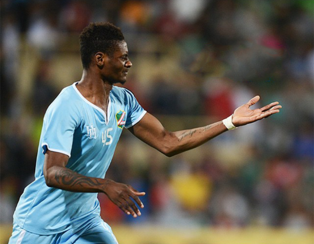 Ein Fußballspieler in einem blauen Trikot feiert mit ausgestreckten Armen, mit einem unscharfen Hintergrund.