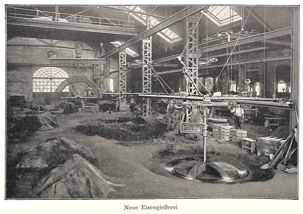 Schwarz-weiß-Fotografie eines Fabrikinneren mit Arbeitern, die an Maschinen arbeiten, umgeben von Metallstangen und -pfählen, beschriftet mit "Neue Eisenglebeerei, die erste Fabrik Deutschlands" unten.