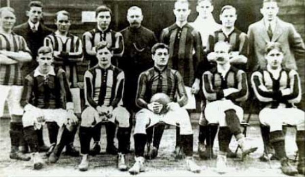 Schwarzes und weißes Foto von Mitgliedern der Ballymena Football Club-Mannschaft, einige stehen, einige sitzen, vor einer Wand.