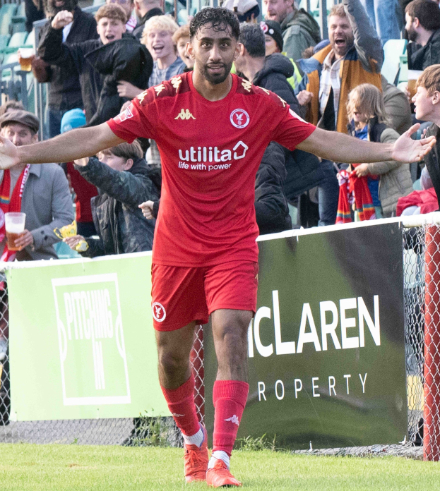Ein Fußballspieler in roter Uniform rennt mit ausgebreiteten Armen auf einem Feld, umgeben von Zuschauern, mit einem Banner im Hintergrund, auf dem 'Middlesbrough FC gegen Swansea City - Sky Bet Championship' steht.