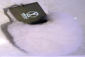 Ein weißer Pelzbeutel mit einem schwarzen Anhänger, aus Schafsfell hergestellt, auf einer weißen Oberfläche.