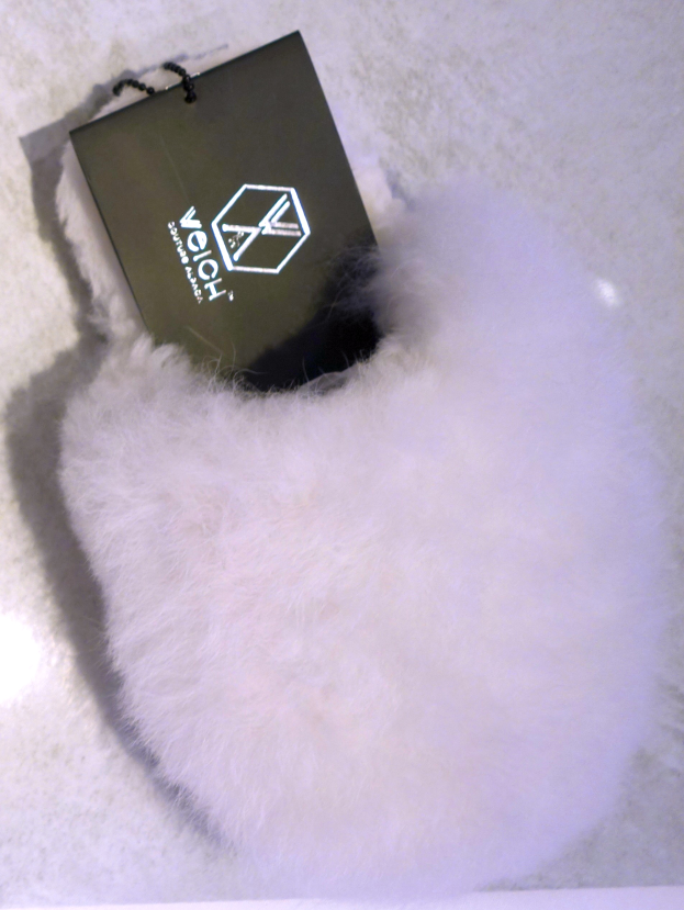 Ein weißer Pelzbeutel mit einem schwarzen Anhänger, aus Schafsfell hergestellt, auf einer weißen Oberfläche.