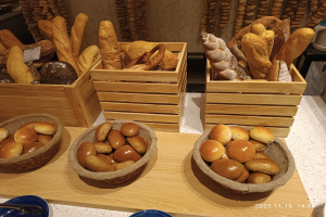 Ein Holztisch präsentiert Körbe mit verschiedenen Brotsorten, Teller und Löffel in einer Pariser Bäckerei mit einer gewässerten Wand im Hintergrund.