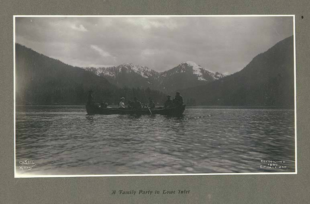 Schwarz-weiß-Foto einer Familie in einem Kanu auf einem See mit Bergen, Bäumen und Himmel im Hintergrund, mit Text unten.