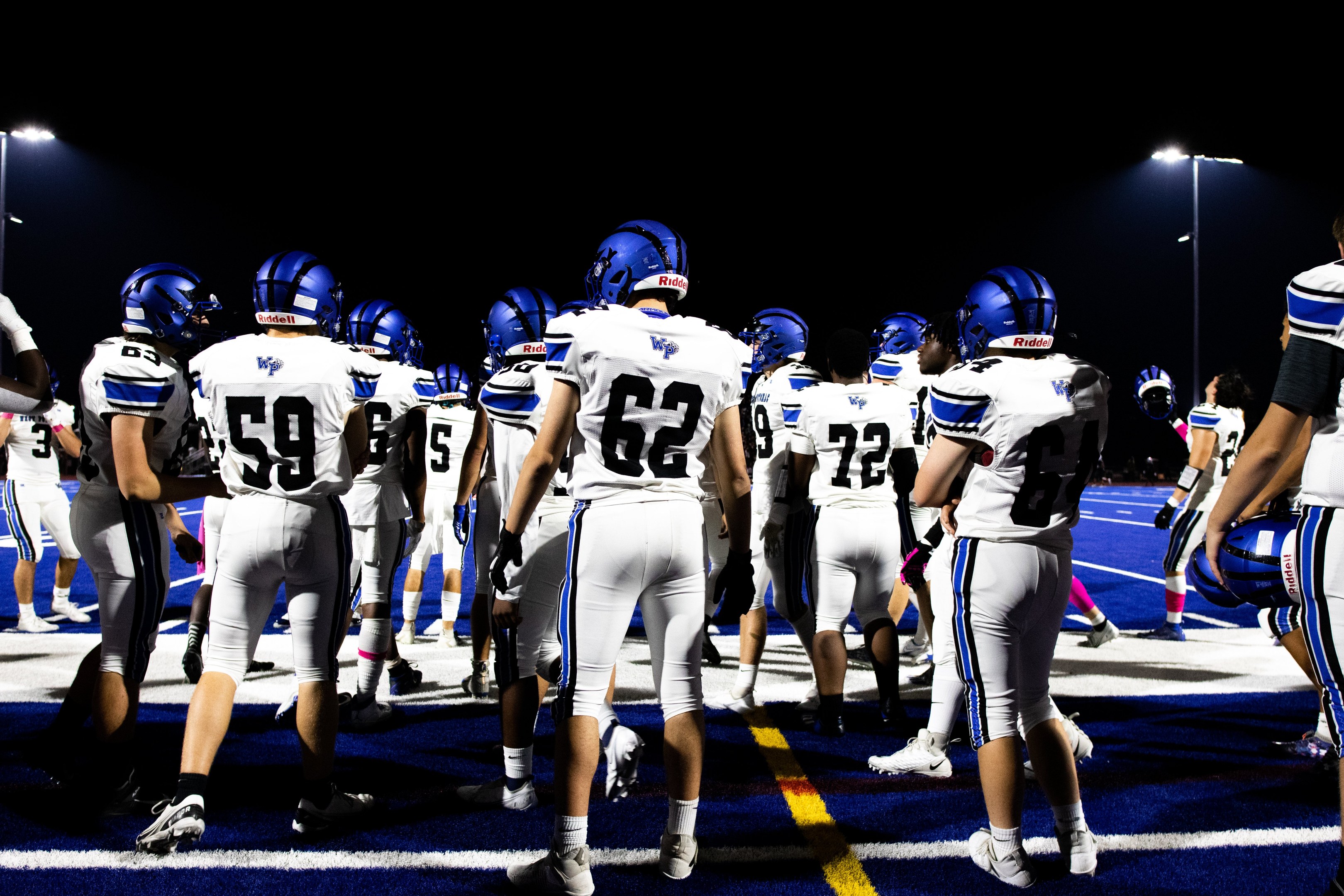 Eine Gruppe von Fußballspielern in Helmen und Stiefeln steht auf einem Feld unter Flutlicht und sieht bereit für ein Spiel aus.