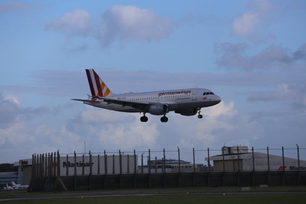 Germanwings Airbus A320-200 beim Start von Frankfurt Airport mit Gras, einem Zaun, Gebäuden, Bäumen und einem bewölkten Himmel im Hintergrund.