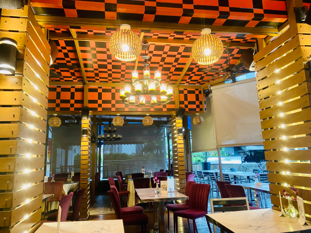 Ein Restaurant-Innenraum mit Tischen und Stühlen unter einer karierten Decke, geschmückt mit Blumenvasen und anderen Dekorationen, während die Wände mit Lampen und Kronleuchtern geschmückt sind.