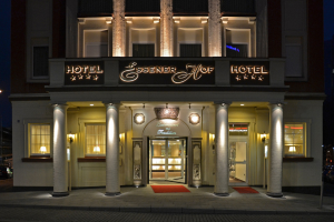 Das Essenerhof Hotel in Berlin, Deutschland, ein mehrstöckiges Gebäude mit Fenstern, Türen, Säulen und einem Namensschild, das entlang einer Straße mit Fahrzeugen auf der rechten Seite und einem sichtbaren Himmel im Hintergrund liegt.