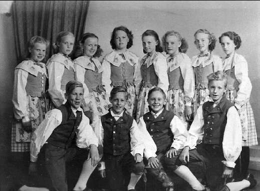Schwarzes und weißes Foto von Kindern, die vor einem Vorhang posieren, mit Text, der unten '1930er Kinder-Schule' liest.