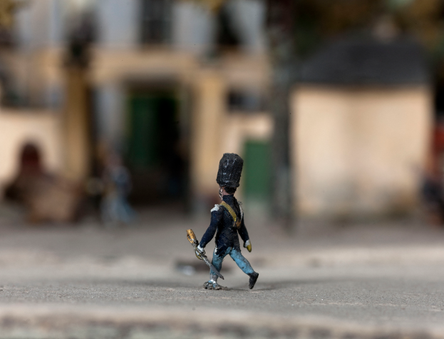 Ein Spielzeugsoldat mit einer Pistole geht die Straße entlang, mit unscharfen Gebäuden im Hintergrund.