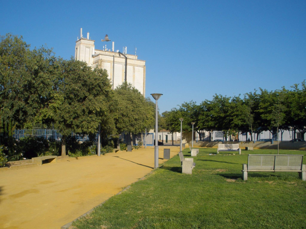 Ein Park mit Bänken und Bäumen vor einem Gebäude, umgeben von Straßenlaternen, Straßenlaternen, Grills, Pflanzen und einem klaren blauen Himmel.