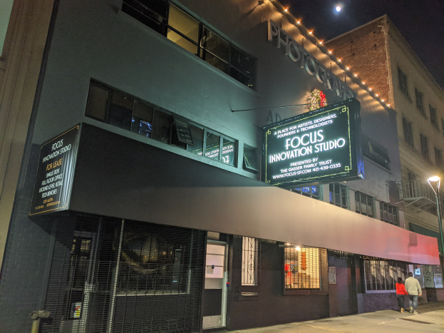 Außenansicht des Focus Innovation Studio in New York City bei Nacht, mit beleuchteten Gebäuden, Menschen auf dem Gehweg und sichtbarem Nachthimmel.