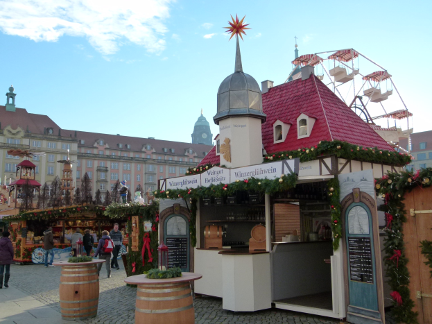 Ein geschäftiger Weihnachtsmarkt in Nürnberg, Deutschland, mit Menschen um Stände herum, die mit Lichtern und Ornamenten geschmückt sind, ein Riesenrad im Hintergrund und eine Tafel mit Text auf der rechten Seite.