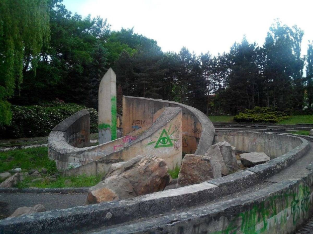 Verlassener Skatepark mit Graffiti an seiner Seite, umgeben von Felsen, Gras, Pflanzen und Bäumen.