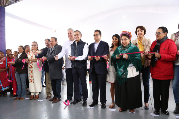 Gruppe von Menschen bei einer Scherenschnitte-Zeremonie mit einer Schere in der Hand, vor einer Menge mit Papieren auf dem Boden und einem weißen Tuch im Hintergrund.