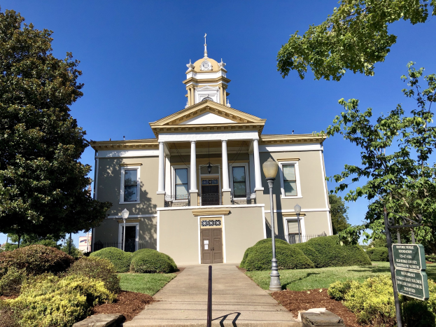 Großes Backsteingebäude mit einem Glockenturm, umgeben von Fenstern, Türen und architektonischen Details, mit Straßenelementen, Grünflächen und einem Schild, als das kürzlich wiedereröffnete alte Rathaus bezeichnet.