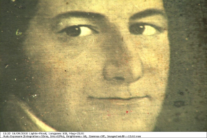 Schwarzes und weißes Foto einer Frau mit zurückgekämmtem Haar, ernstem Gesichtsausdruck, direktem Blick und leichtem Lächeln, mit Text unten.