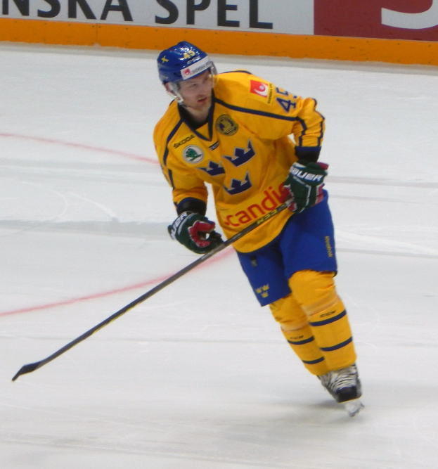Ein Eishockeyspieler in Bewegung auf dem Eis, der einen Helm, Handschuhe und Schlittschuhe trägt und einen Hockeystock hält, mit einer textgefüllten Tafel im Hintergrund.