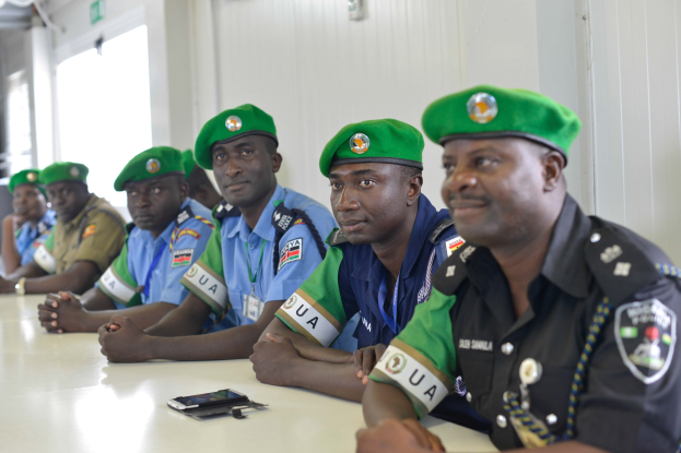 Eine Gruppe von Polizisten sitzt an einem Tisch während einer Schulung, mit Mobiltelefonen und anderen Gegenständen auf dem Tisch, in einem Raum mit Fenstern und Deckenleuchten.