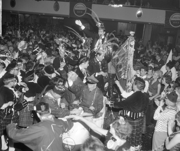 Ein Schwarz-Weiß-Bild einer Menge von Menschen in Kilts, die auf einer Party tanzen, wobei einige Musikinstrumente und Schilder halten.