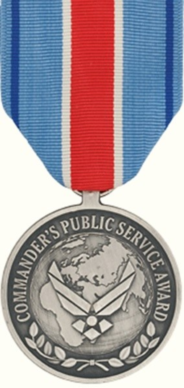 Eine silberne Medaille mit einer rot-weiß-blauen Schleife, die den Text 'Commander's Public Service Award' auf einem weißen Hintergrund zeigt.