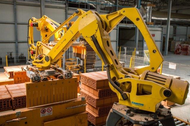 Großes Industriegebäude mit gestapelten Kisten, Kränen, Zaun, Pfählen und einer fernen Wand in einer Fertigungsumgebung.