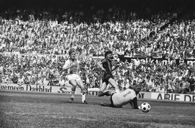 Schwarz-weißes Foto von Männern, die auf einem Feld Fussball spielen, mit Zuschauern im Hintergrund und einer Bundesliga 1978-79 Ajax 1-1 Hannover 96-Banner.