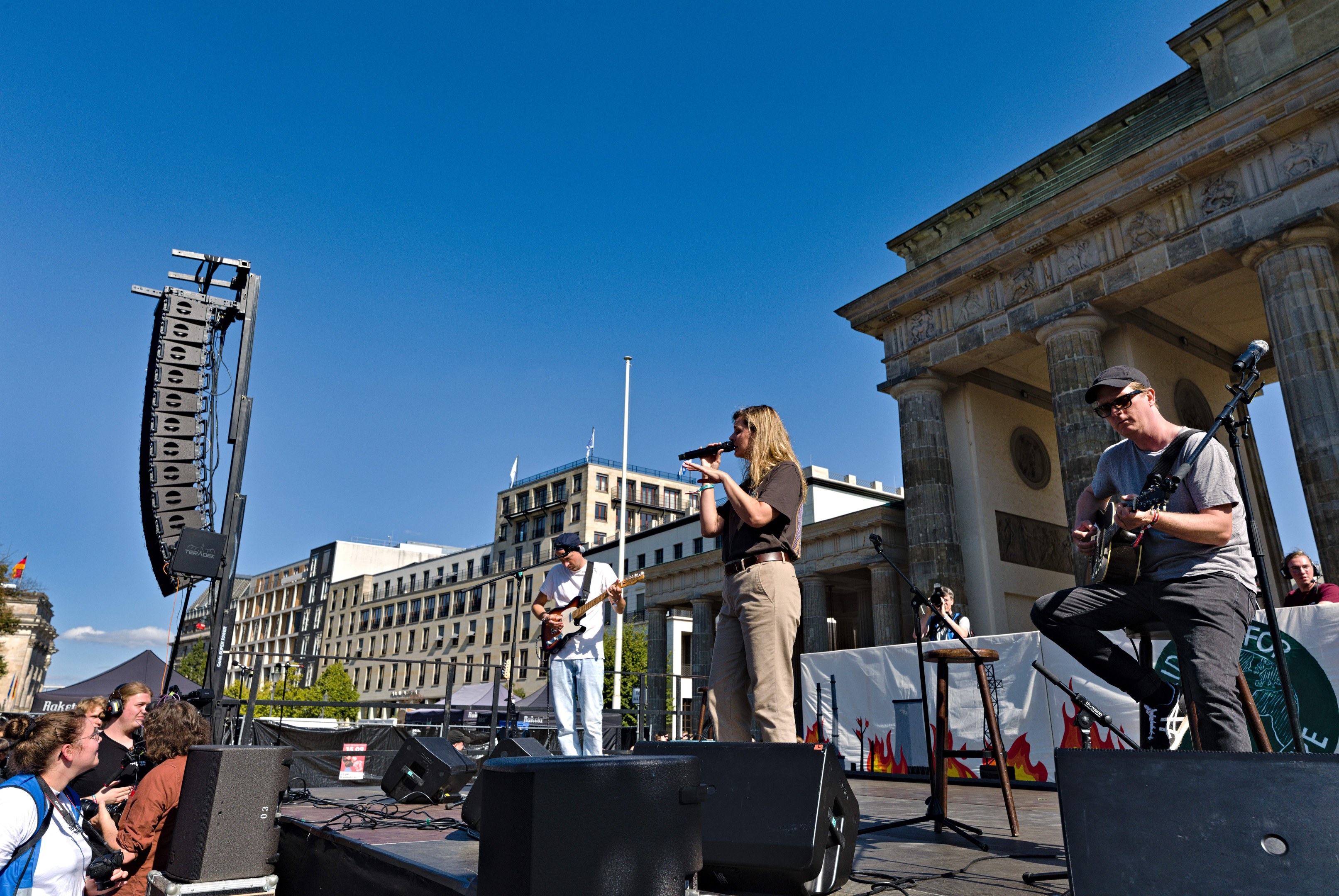 Eine Gruppe von Menschen, die auf einer Bühne vor dem Brandenburger Tor in Berlin spielen und singen.