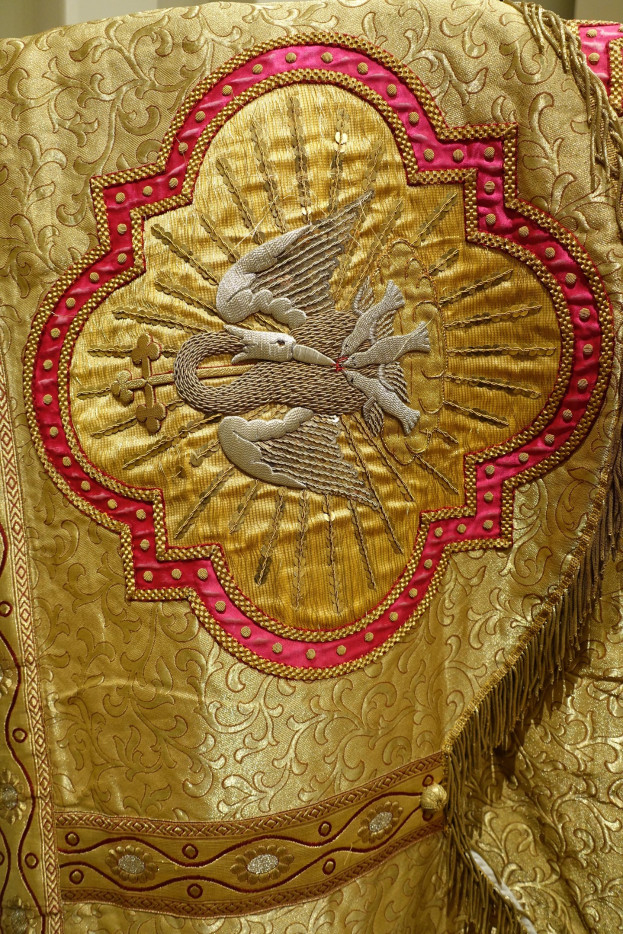 Nahaufnahme eines Priestergewandes mit goldenen und roten Stickereien vor einem Wandhintergrund.