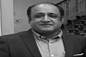 Ein Mann in einem Anzug steht vor einer Treppe, sieht besorgt aus, mit einer Wand im Hintergrund, dargestellt in Schwarz-Weiß.