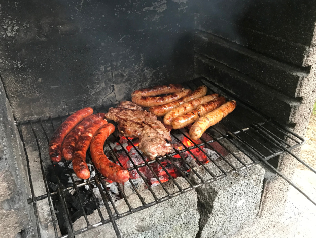 Grill mit Würstchen und Fleisch auf Kohle und Flammen, im Freien auf Gras.
