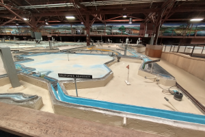 Ein großes Indoor-Wasserpark mit zahlreichen Wasserrutschen, Pfosten, Texttafeln, Deckenleuchten und Wandgemälden, das wie ein Miniatur-Golfplatz für einen spaßigen und aufregenden Erlebnis designed ist.