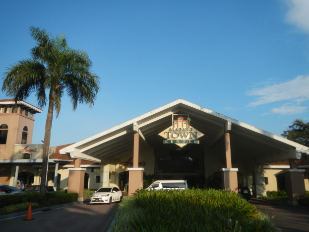 Der Eingang eines Resorts mit Palmen vorne, umgeben von Gebäuden, Kraftfahrzeugen auf der Straße, Verkehrskegel, Büschen, Bäumen und einem bewölkten Himmel im Hintergrund.