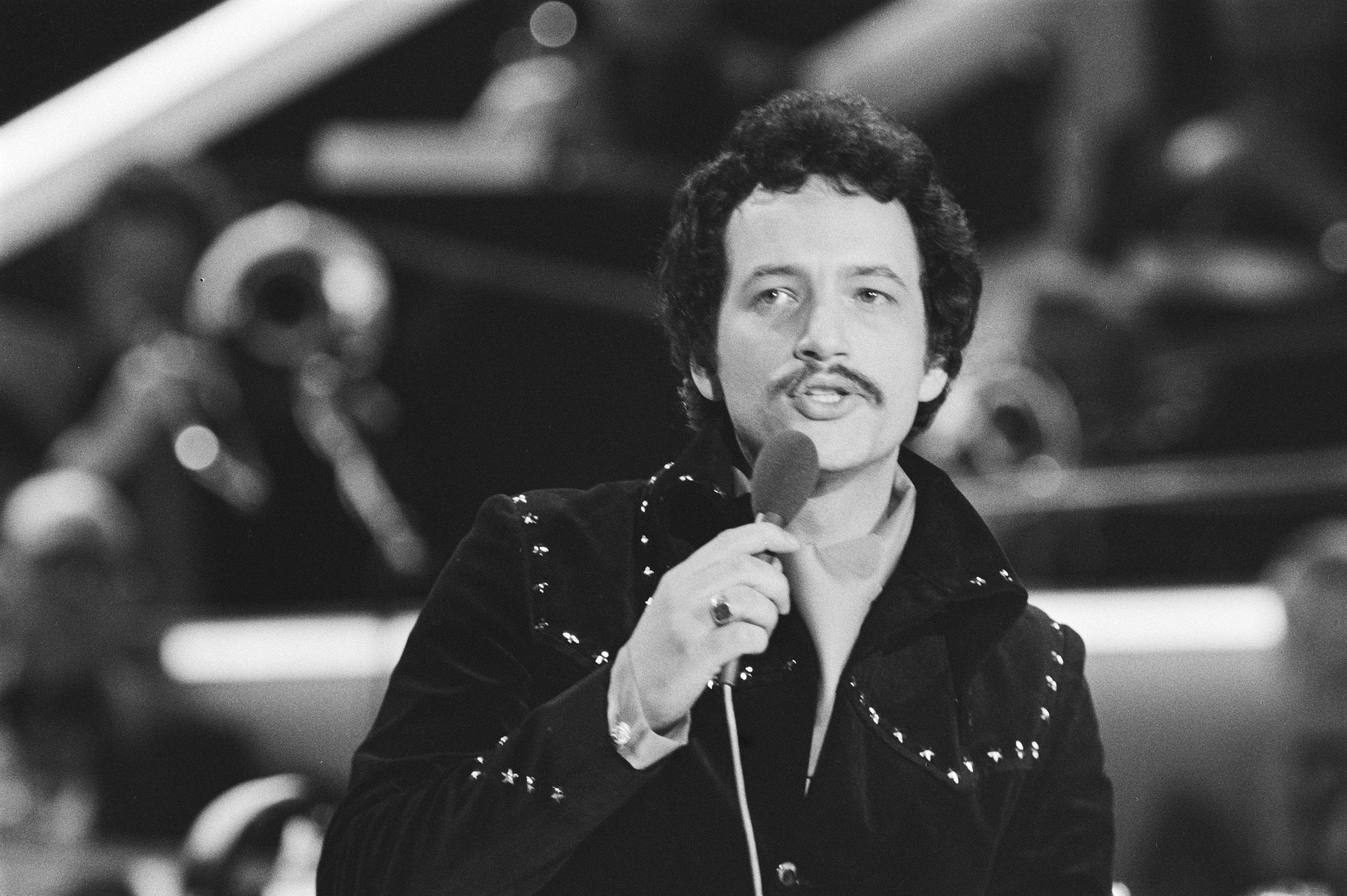 Schwarzes und weißes Foto von Elvis Presley mit einem Mikrofon bei einer Live-Aufführung.