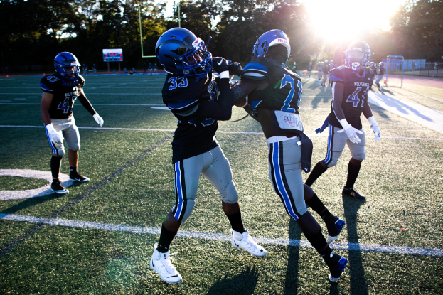 Gruppe junger Männer in Helmen und Fußballkleidung auf einem Feld mit Bäumen und einem klaren blauen Himmel.