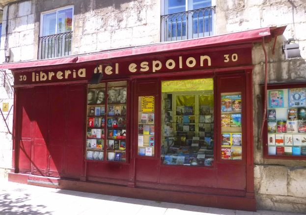Ein rotes Schirmbuchgeschäft namens "Libreria del Espolon" mit ordentlich sortierten Büchern im Inneren, das sich in einem Gebäude mit Fenstern und Geländern befindet.