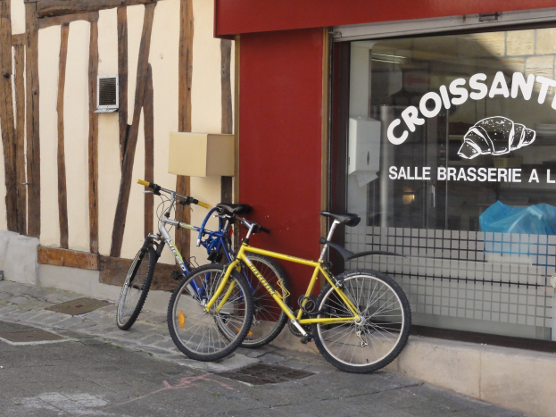 Zwei Fahrr├Ąder nebeneinander auf einem Gehweg vor einem Laden mit einer Glaswand, auf der Text und ein Objekt zu sehen ist.