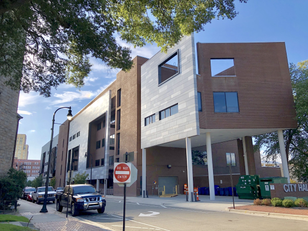 Großes Gebäude mit der Bezeichnung "Stadthallen Apartments" mit vielen Fenstern, umgeben von Straßeninfrastruktur einschließlich Pfosten, Lampen, Fahrzeugen, Schildern und Verkehrselementen, mit Bäumen und einem bewölkten Himmel im Hintergrund.