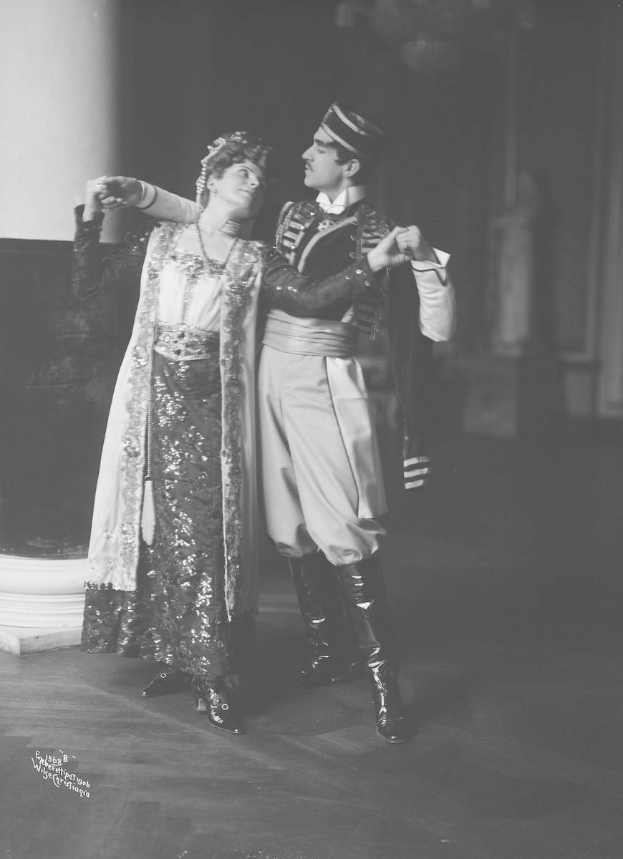 Schwarzes und weißes Foto eines Mannes und einer Frau, die in einem Ballsaal tanzen, mit einer Säule und einer Wand im Hintergrund; der Mann trägt Schuhe, was auf eine Vorstellung hindeutet.