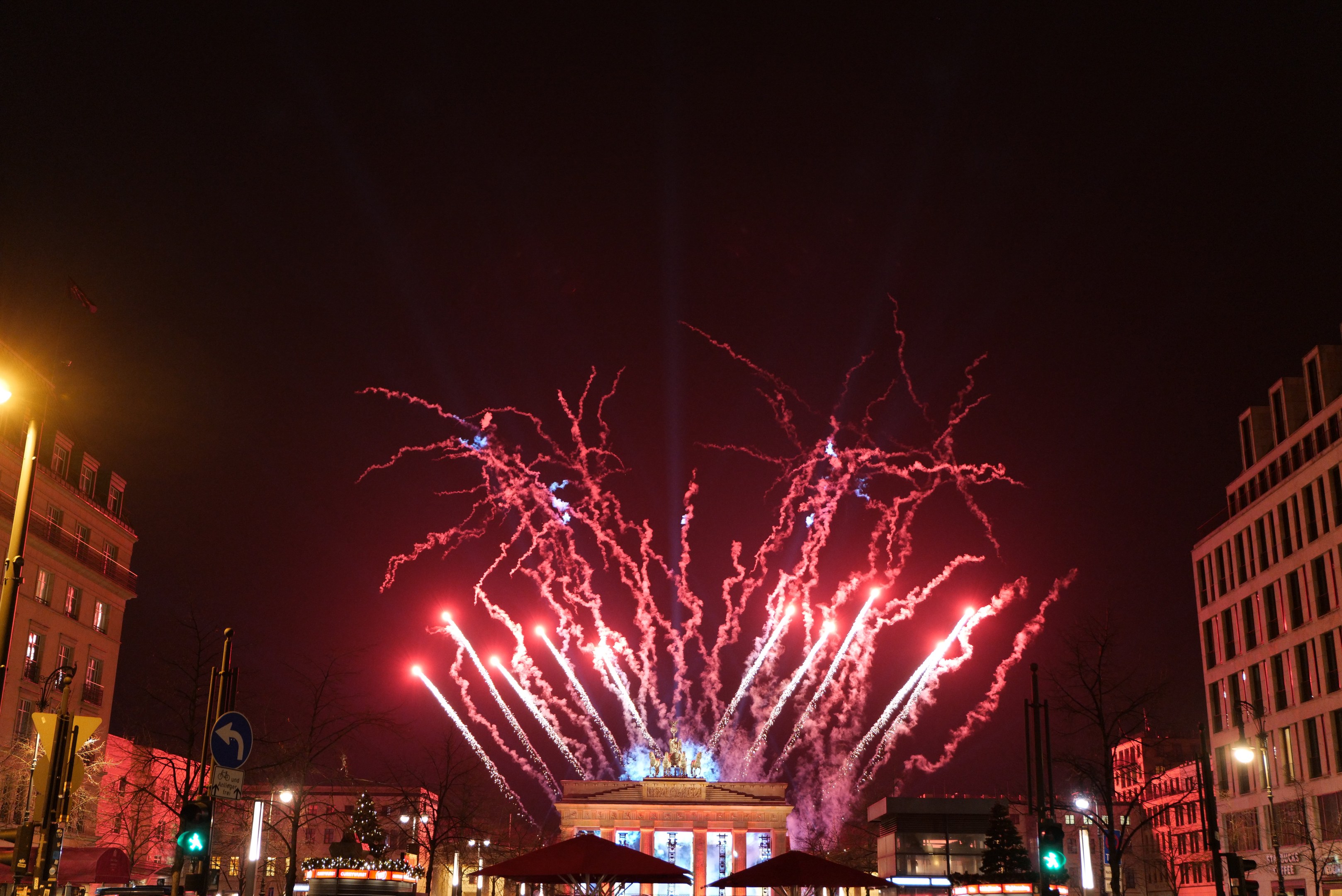 Eine belebte Straßen in Berlin an Silvester, voller Menschen, Fahrzeuge und festlicher Lichter von Gebäuden und Feuerwerk am Himmel.