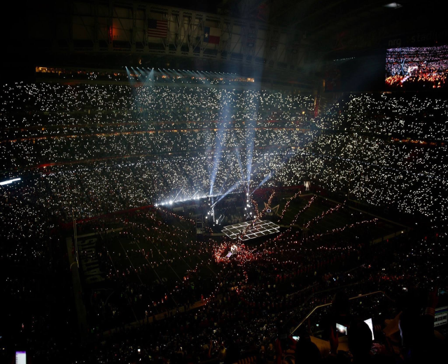 Gro├čes Publikum in einem hell erleuchteten Stadion bei Nacht mit einem Bildschirm, der die Ergebnisse der Super Bowl XLVII-Halbzeit auf der rechten Seite anzeigt.