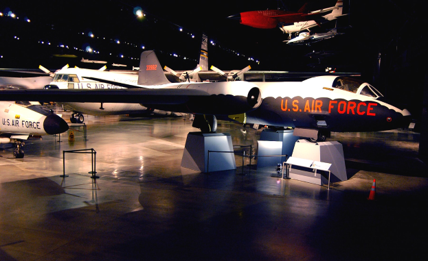 Eine Gruppe von Kampfflugzeugen in einem schwach beleuchteten Museum mit St├Ąnden, Verkehrskegeln und anderen Bodenobjekten im Hintergrund.