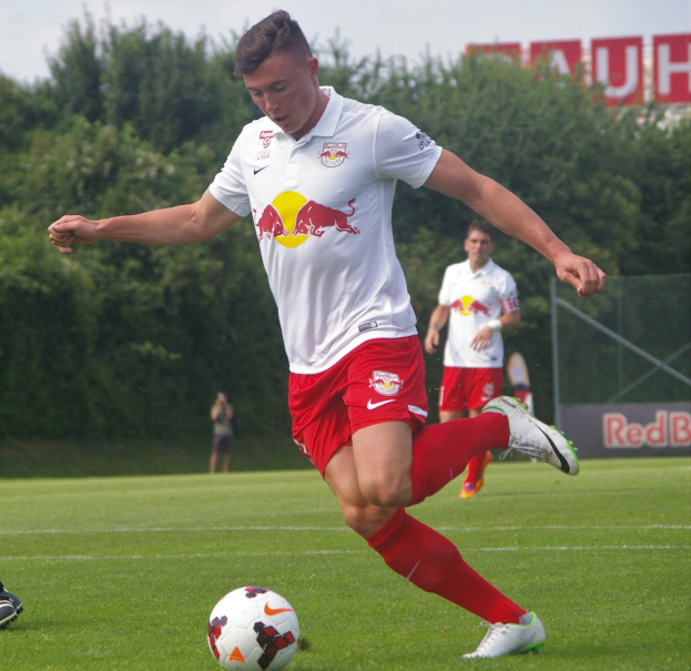 Ein professioneller Fussballspieler tritt einen Ball auf einem grünen Feld mit «RB Leipzig» im Hintergrund.