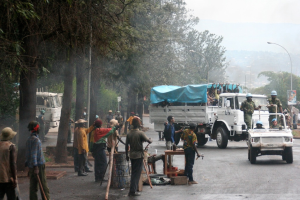 Arbeiter führen Aufgaben neben einer Straße mit einem Lastwagen durch, der eine große Menge trägt, während Beamte in einem Fahrzeug in der Nähe fahren, umgeben von Bäumen und Straßenlaternen.