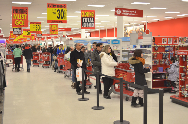 Ein volles Walmart-Geschäft mit Einkaufswagen schiebenden Kunden und Menschen mit Taschen, umgeben von Warenpräsentationen, Schildern und Deckenleuchten.